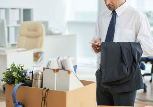 unrecognizable-man-standing-office-using-smartphone-with-personal-belongings-box_11zon
