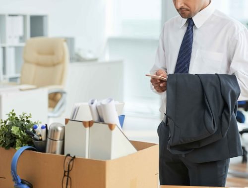 unrecognizable-man-standing-office-using-smartphone-with-personal-belongings-box_11zon
